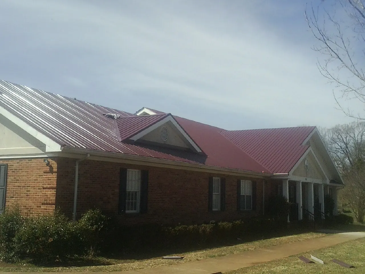 Red metal roof with gabled entries on a long brick building, from a Hail Damage Roof Repair job in Annapolis