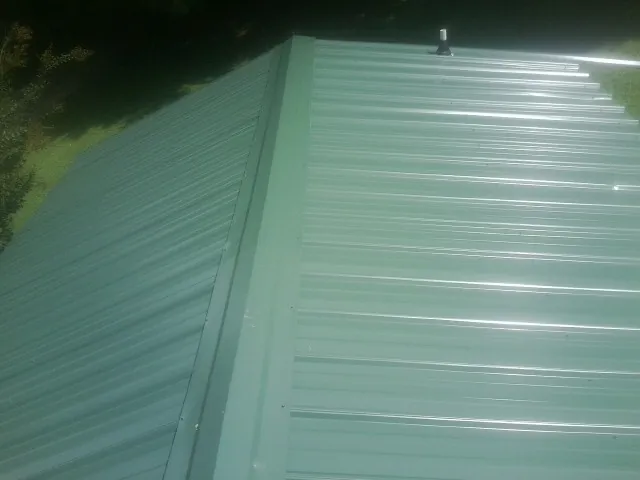 New green metal panels meeting at the ridge of a roof — Flat Roof Repair work by our crew in Annapolis